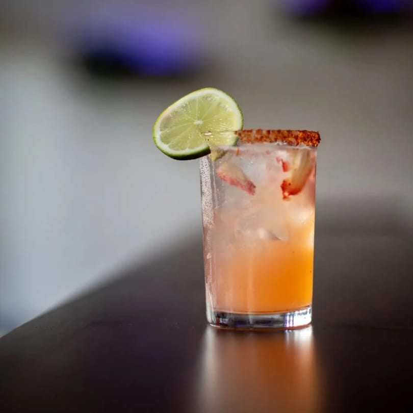 A Highline Park strawberry margarita with a chili-lime rim and a lime wedge on a dark bar.