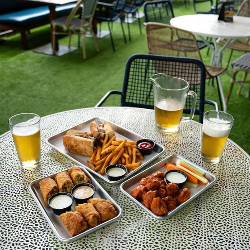 Highline Park outdoor patio with bar-&-grill food, including wings, fries, and egg rolls, with beers.