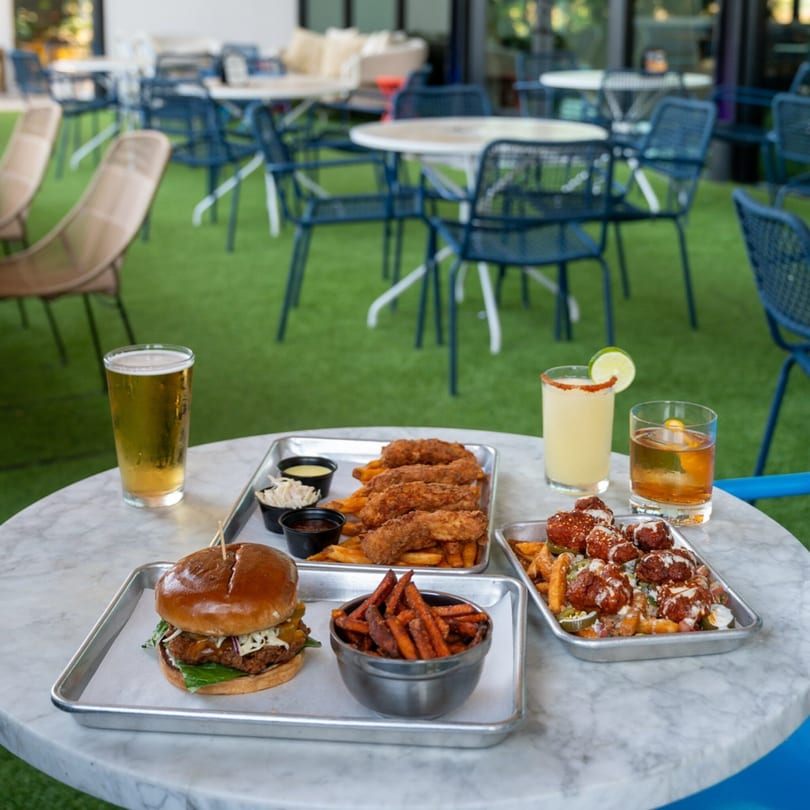 Highline Park outdoor dining with a burger, chicken tenders, fries, and drinks on a marble table.
