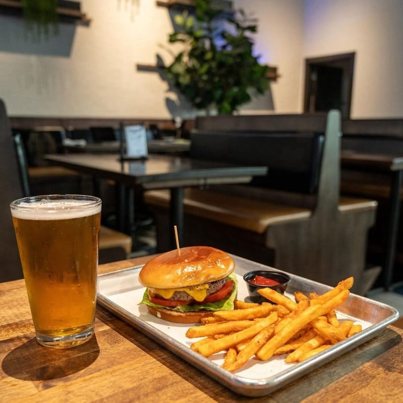 Highline Park's burger and fries with a beer on a wooden table in a restaurant setting.