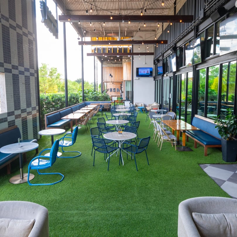 Highline Park's outdoor patio features artificial turf, blue seating, and string lights under a covered ceiling.