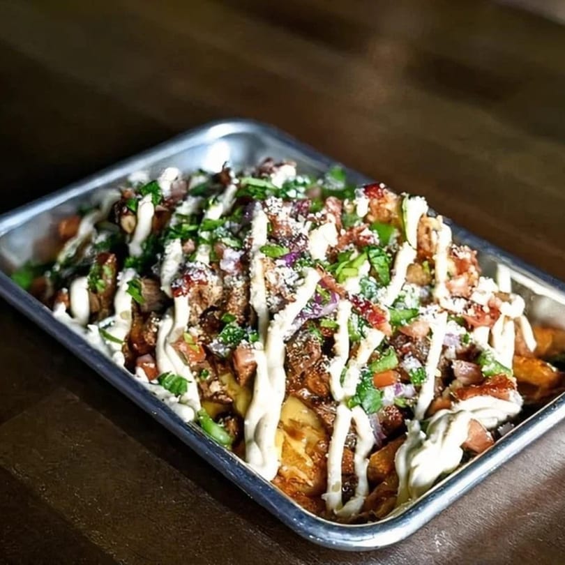 Highline Park's loaded fries with meat, cheese, sauce, and herbs in a metal tray.