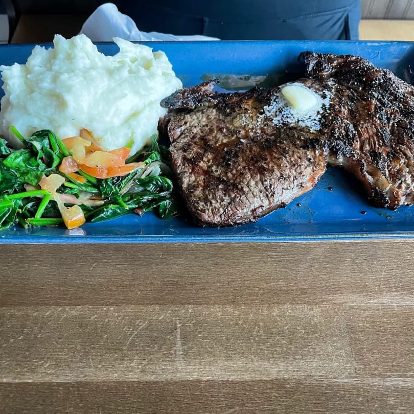 Grilled steak with a pat of butter, mashed potatoes, and sautéed spinach on a blue plate.