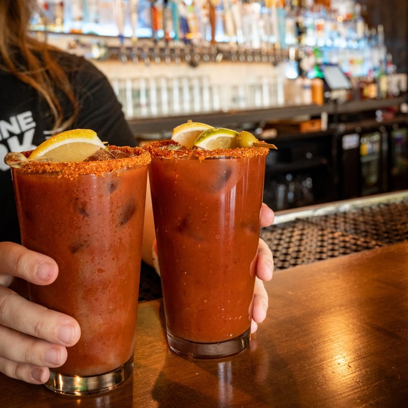 Two Bloody Mary cocktails with lemon and lime garnishes, served by a bartender at Highline Park.