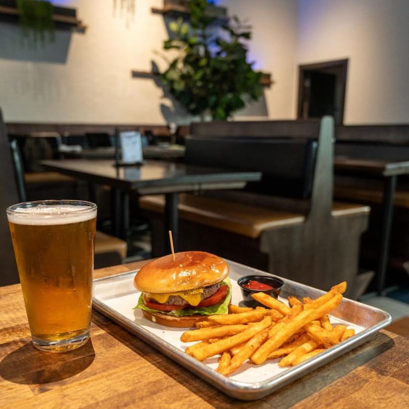 Highline Park's cheeseburger and fries with a beer on a wooden table in a restaurant setting.